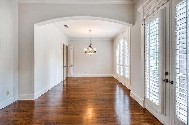 empty room featuring an inviting chandelier, plenty of natural light, dark hardwood / wood-style floors, and ornamental molding