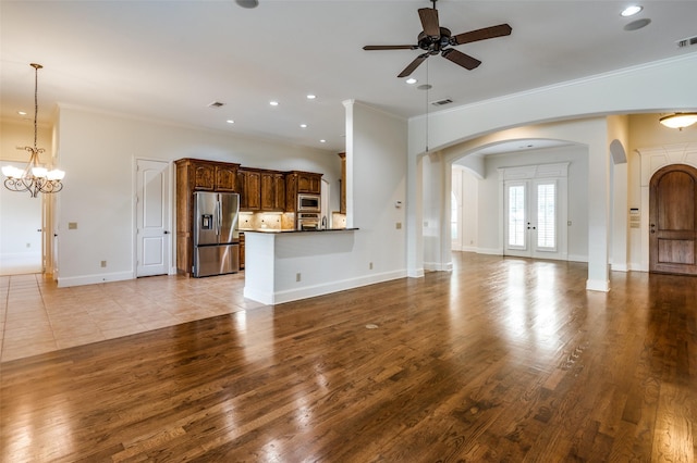 unfurnished living room with crown molding, light wood-type flooring, ceiling fan with notable chandelier, and french doors