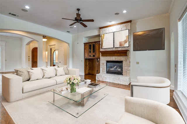 living room featuring ceiling fan, hardwood / wood-style floors, ornamental molding, and a stone fireplace