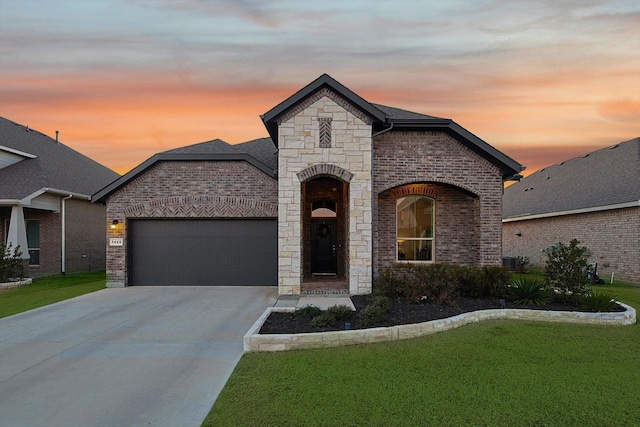 french country home featuring brick siding, central air condition unit, concrete driveway, a yard, and a garage