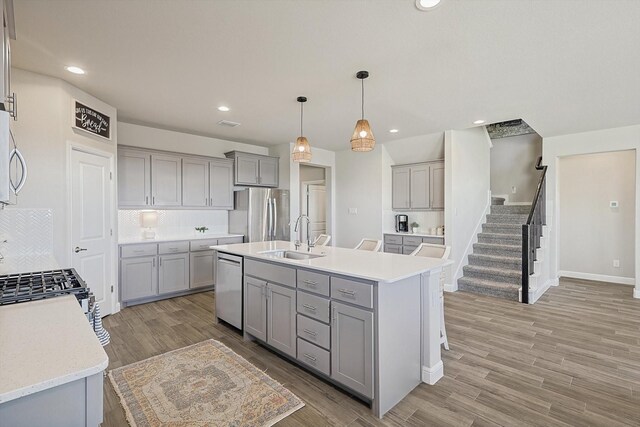 kitchen with sink, gray cabinets, pendant lighting, stainless steel appliances, and light hardwood / wood-style floors