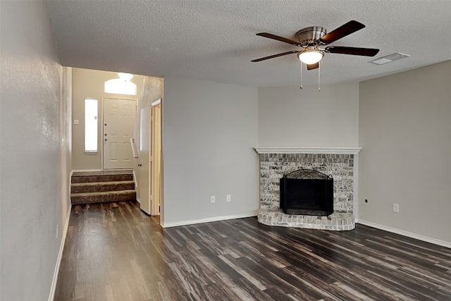 unfurnished living room featuring ceiling fan, a textured ceiling, a brick fireplace, and dark hardwood / wood-style flooring