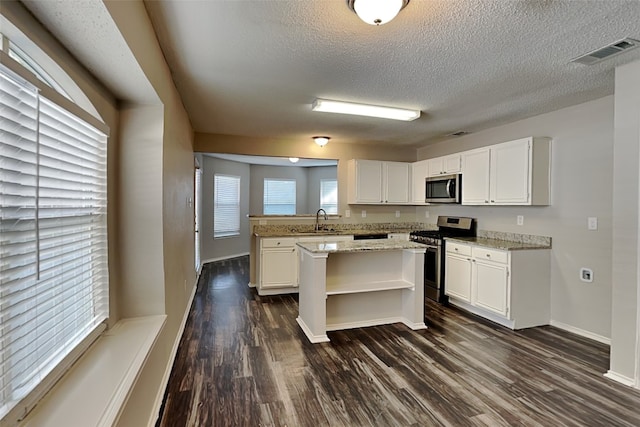 kitchen featuring appliances with stainless steel finishes, sink, white cabinetry, light stone countertops, and a kitchen island