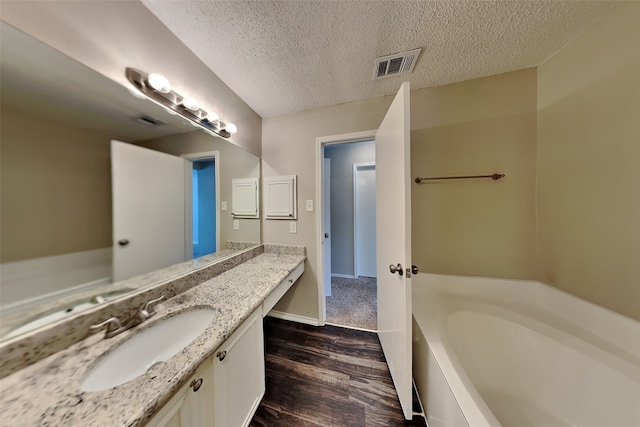 bathroom with a textured ceiling, vanity, hardwood / wood-style floors, and a bath