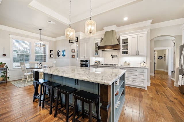 kitchen featuring custom exhaust hood, white cabinetry, hanging light fixtures, and a large island