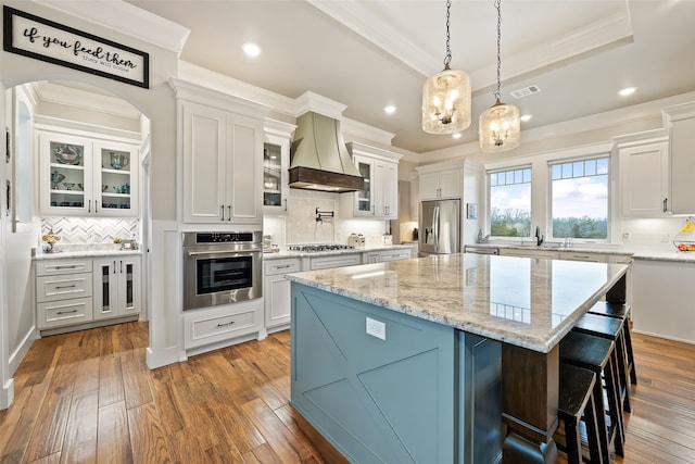 kitchen featuring custom exhaust hood, white cabinetry, appliances with stainless steel finishes, and a center island