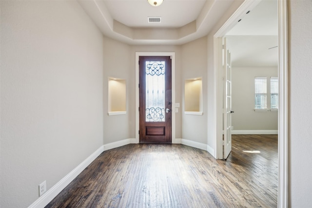 foyer featuring a tray ceiling, visible vents, baseboards, and wood finished floors