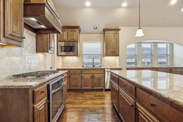 kitchen featuring light stone counters, dark wood-style flooring, custom exhaust hood, stainless steel appliances, and a sink