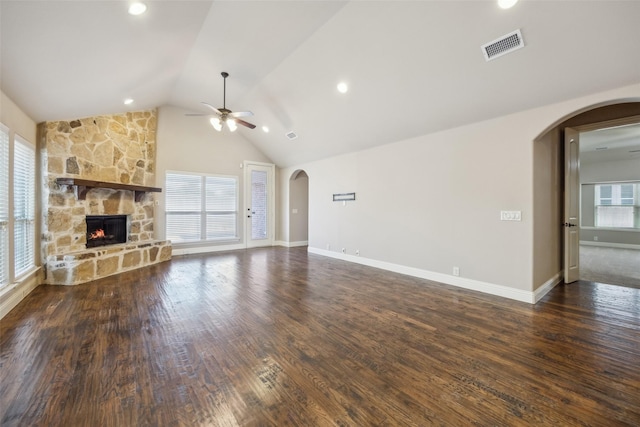 unfurnished living room featuring arched walkways, dark wood-style flooring, plenty of natural light, and a stone fireplace