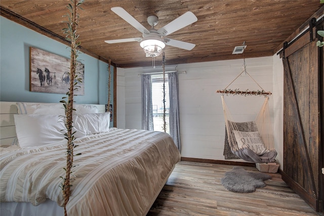 bedroom featuring ceiling fan, a barn door, light hardwood / wood-style flooring, and wooden ceiling