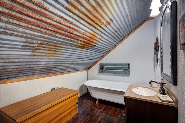 bathroom featuring hardwood / wood-style floors, wooden walls, vanity, vaulted ceiling, and a tub