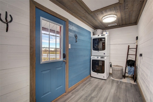 laundry room with wood ceiling, stacked washing maching and dryer, wood walls, and hardwood / wood-style floors