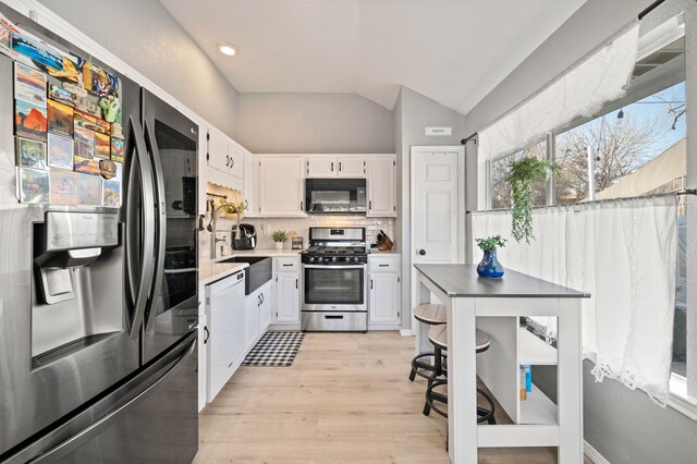 kitchen featuring stainless steel appliances, white cabinetry, vaulted ceiling, and backsplash