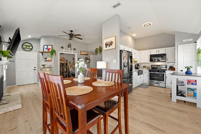 dining space with ceiling fan, a fireplace, lofted ceiling, and light wood-type flooring