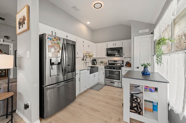 kitchen featuring light hardwood / wood-style flooring, vaulted ceiling, appliances with stainless steel finishes, backsplash, and white cabinets