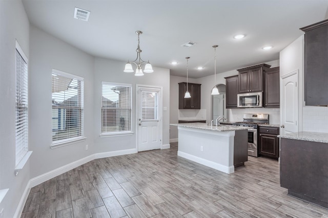 kitchen featuring light stone countertops, tasteful backsplash, dark brown cabinetry, pendant lighting, and stainless steel appliances