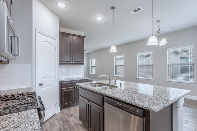 kitchen with dark brown cabinetry, stainless steel appliances, an island with sink, decorative backsplash, and sink