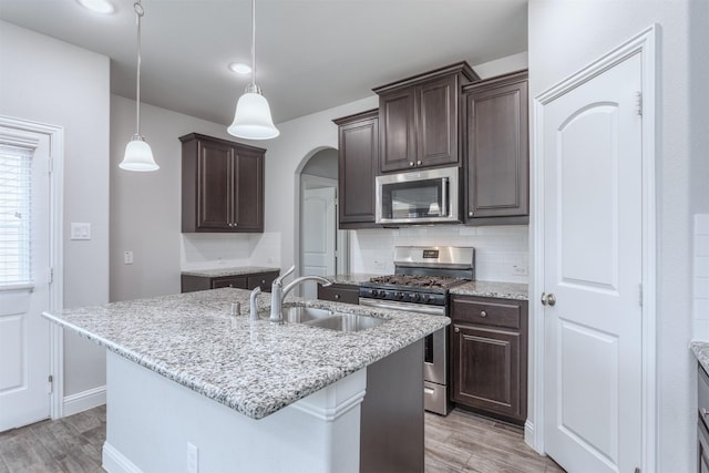 kitchen with a kitchen island with sink, sink, light wood-type flooring, backsplash, and stainless steel appliances