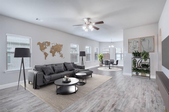 living room featuring ceiling fan with notable chandelier and light hardwood / wood-style flooring