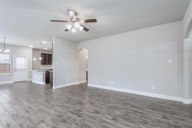 unfurnished living room featuring ceiling fan with notable chandelier, sink, and dark hardwood / wood-style floors