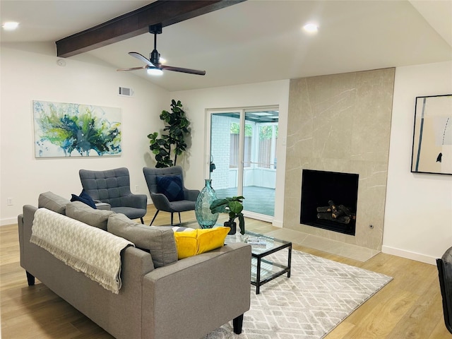 living room with a tile fireplace, light hardwood / wood-style flooring, vaulted ceiling with beams, and ceiling fan