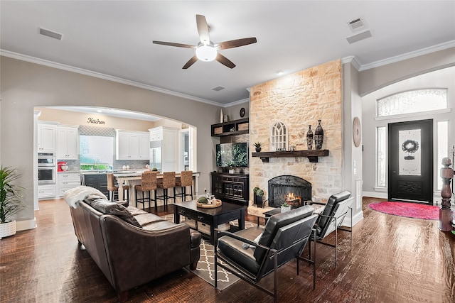 living room with crown molding, hardwood / wood-style flooring, ceiling fan, and a stone fireplace