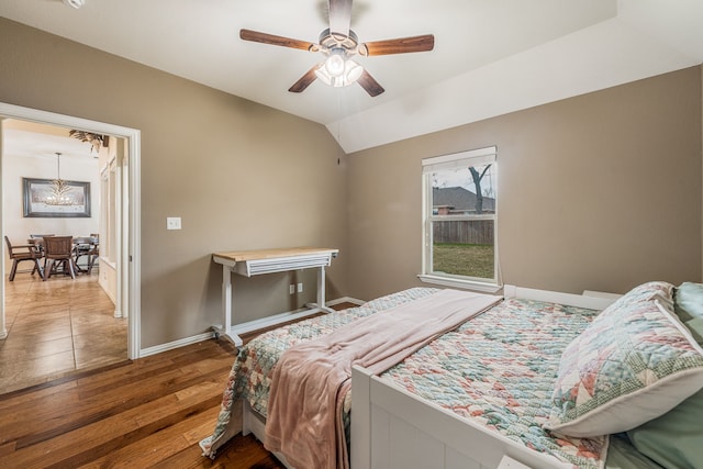 bedroom featuring ceiling fan with notable chandelier, hardwood / wood-style flooring, and vaulted ceiling