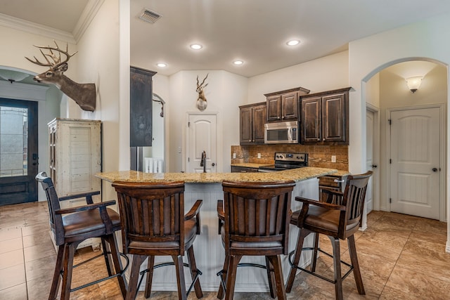 kitchen with light stone countertops, appliances with stainless steel finishes, tasteful backsplash, ornamental molding, and a breakfast bar