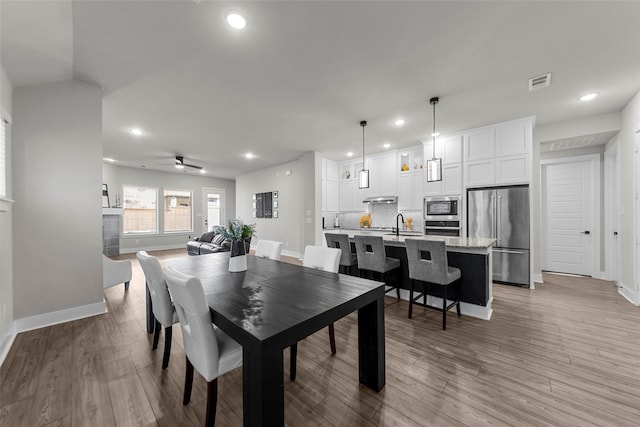 dining space featuring a fireplace, light hardwood / wood-style flooring, sink, and ceiling fan