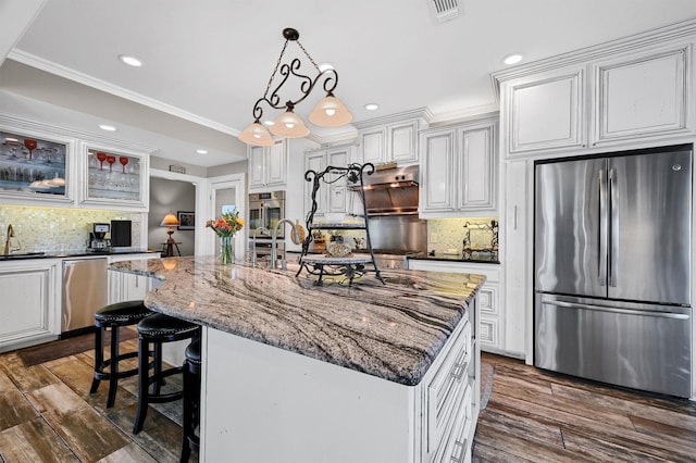 kitchen with white cabinets, appliances with stainless steel finishes, dark stone counters, an island with sink, and hanging light fixtures