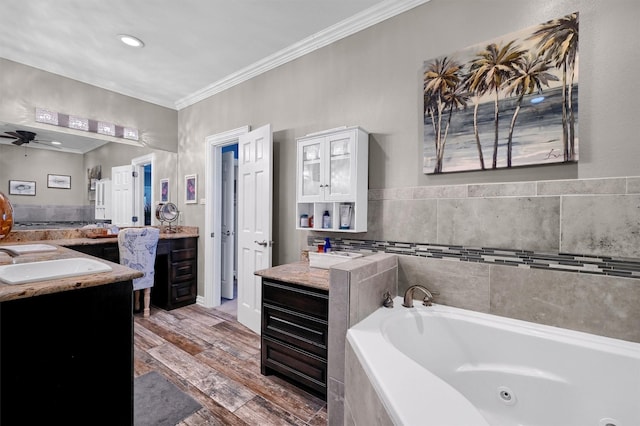 bathroom with ceiling fan, tiled tub, vanity, and ornamental molding