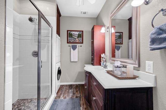 bathroom with hardwood / wood-style floors, a shower with door, stacked washing maching and dryer, and vanity