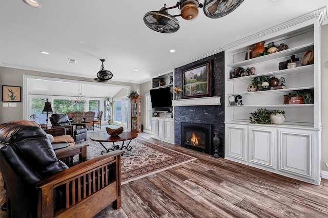 living room with wood-type flooring, built in shelves, ornamental molding, a notable chandelier, and a large fireplace