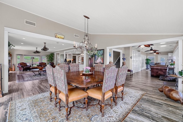 dining room with ceiling fan with notable chandelier, wood-type flooring, and lofted ceiling