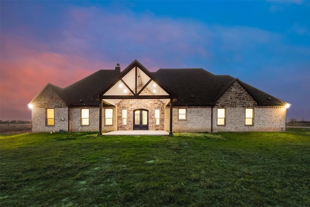 back house at dusk featuring french doors, a patio area, and a lawn