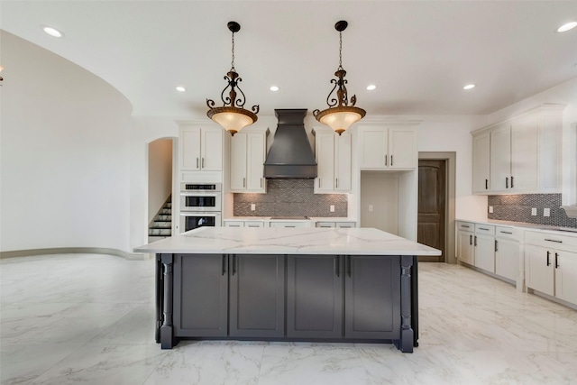 kitchen featuring a large island, hanging light fixtures, white cabinets, and premium range hood