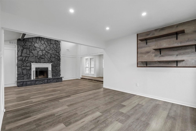 unfurnished living room featuring wood-type flooring, beamed ceiling, and a stone fireplace