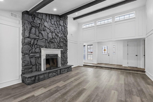 unfurnished living room featuring wood-type flooring, lofted ceiling with beams, and a stone fireplace