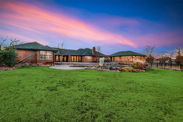 back house at dusk featuring a patio area and a yard