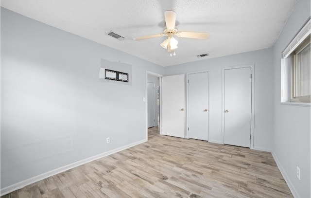 unfurnished bedroom featuring ceiling fan, light hardwood / wood-style floors, a textured ceiling, and multiple closets