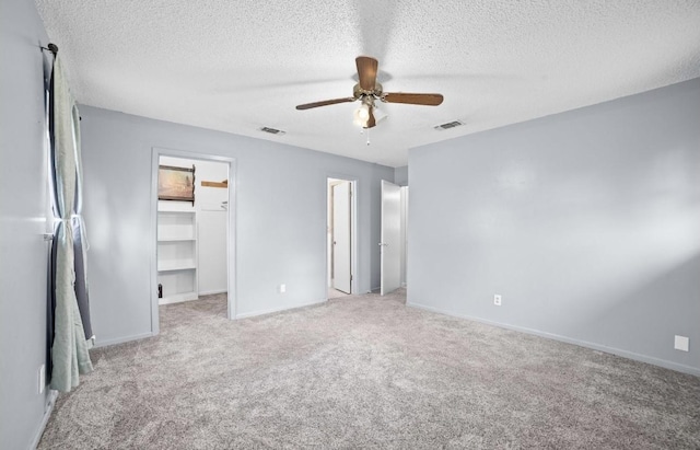 unfurnished bedroom with a spacious closet, a textured ceiling, light carpet, a closet, and ceiling fan