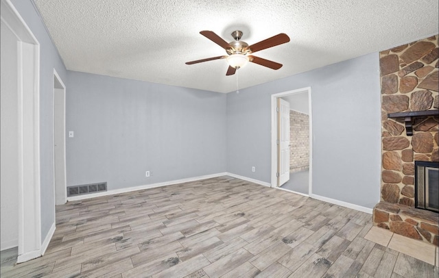 unfurnished bedroom with ceiling fan, a textured ceiling, light hardwood / wood-style flooring, and a stone fireplace