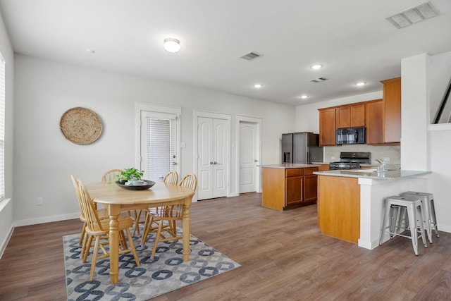 kitchen featuring black appliances, hardwood / wood-style flooring, decorative backsplash, kitchen peninsula, and a breakfast bar