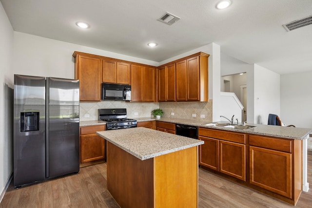 kitchen with sink, light stone counters, light hardwood / wood-style floors, a center island, and black appliances