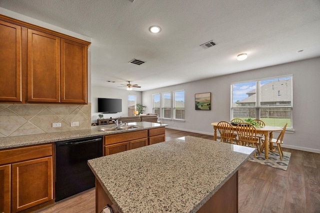 kitchen with sink, tasteful backsplash, light stone countertops, a center island, and black dishwasher