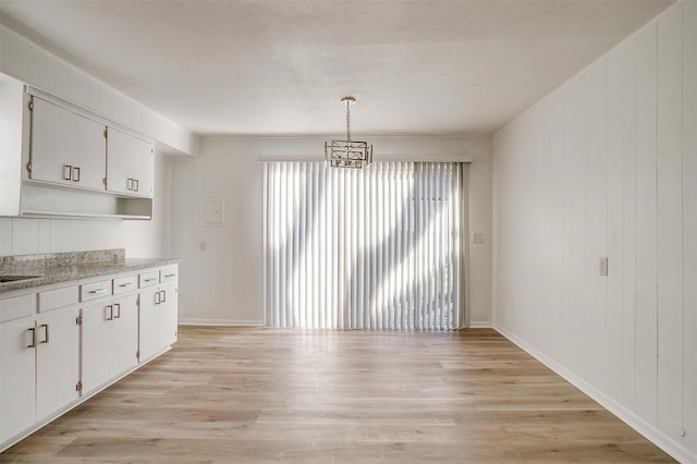 unfurnished dining area with an inviting chandelier, a textured ceiling, and light wood-type flooring