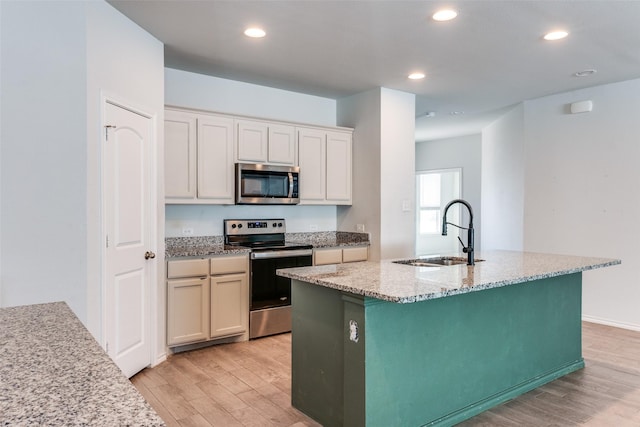 kitchen with light hardwood / wood-style floors, appliances with stainless steel finishes, sink, and a kitchen island with sink