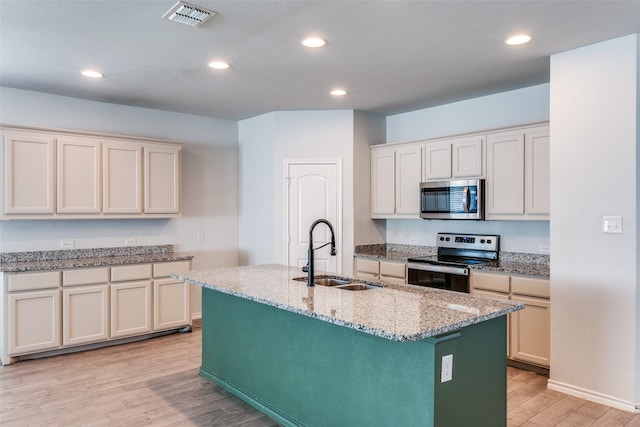 kitchen with a center island with sink, light hardwood / wood-style floors, sink, light stone counters, and appliances with stainless steel finishes