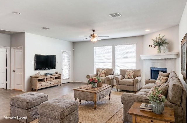 living room with hardwood / wood-style floors, a tiled fireplace, and ceiling fan