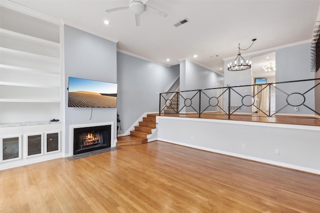 unfurnished living room with built in shelves, ceiling fan with notable chandelier, light hardwood / wood-style flooring, and ornamental molding